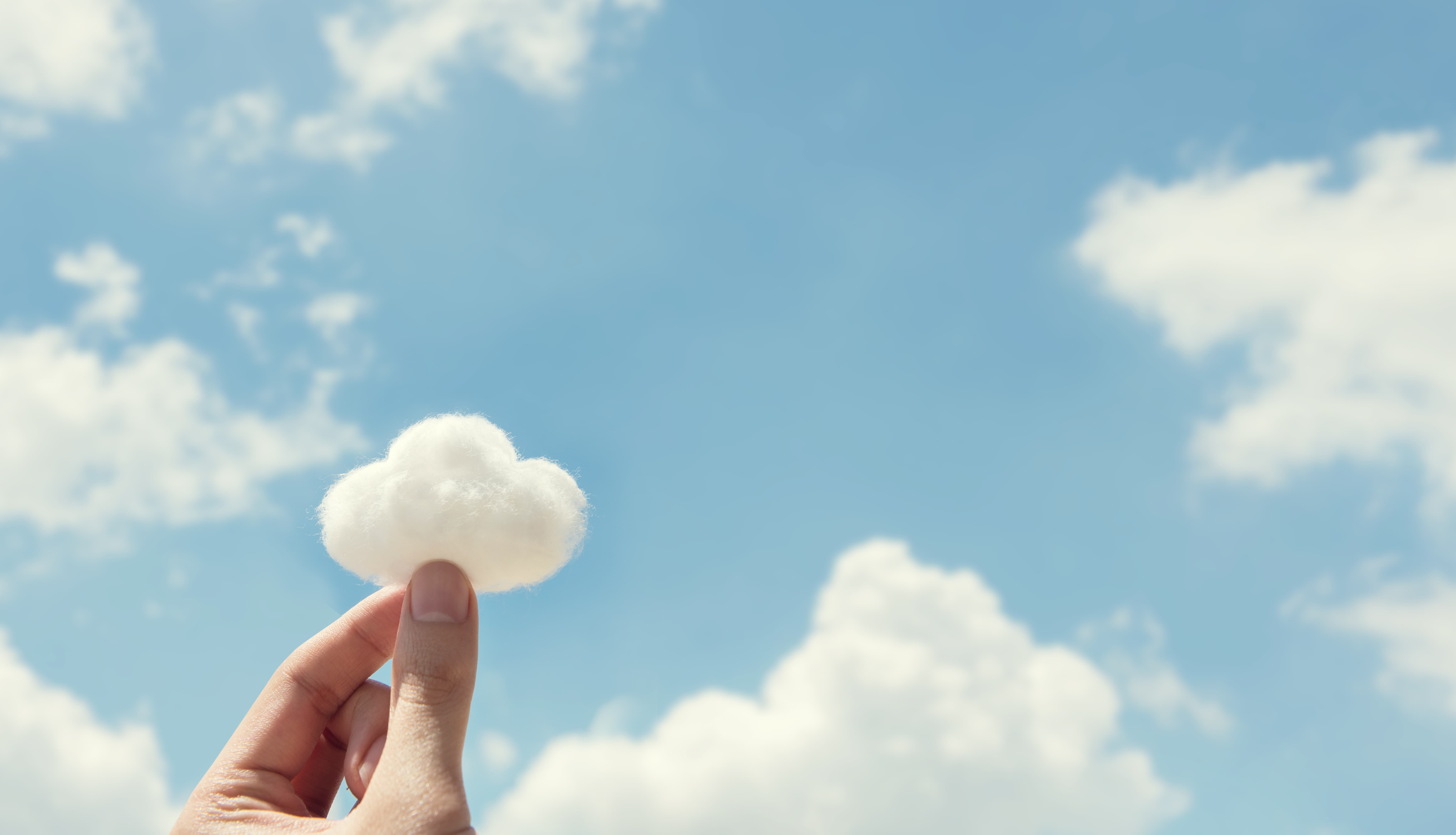 Blue sky with clouds and one cloud from cotton wool held by two fingertips